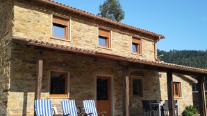 Un bâtiment en pierre avec un toit en tuiles, un patio couvert avec des chaises longues à rayures et une table avec des chaises.