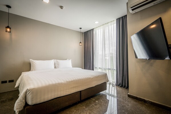 Une chambre d’hôtel moderne dotée d’un grand lit, d’un téléviseur à écran plat fixé au mur et d’une grande fenêtre avec des rideaux.
