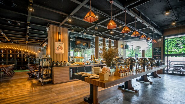 Ein Café mit einer langen Holztresen, hängenden Pendelleuchten und Blick auf Grünflächen.