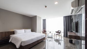 Quarto de hotel moderno com uma cama grande, uma escrivaninha, uma cadeira, uma televisão e uma varanda com cortinas.