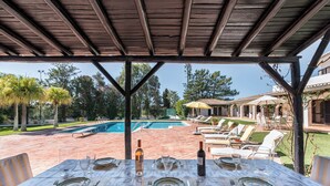 Un espace extérieur aménagé pour les repas, avec une piscine et des chaises longues en arrière-plan.