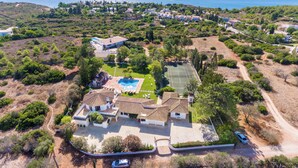 Vue aérienne d’un quartier résidentiel avec une grande maison dotée d’une piscine, d’un court de tennis et d’une allée où sont garées des voitures.