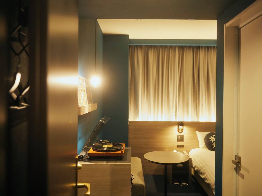 Una habitación de hotel con una cama, una mesita, una lámpara y un tocadiscos.