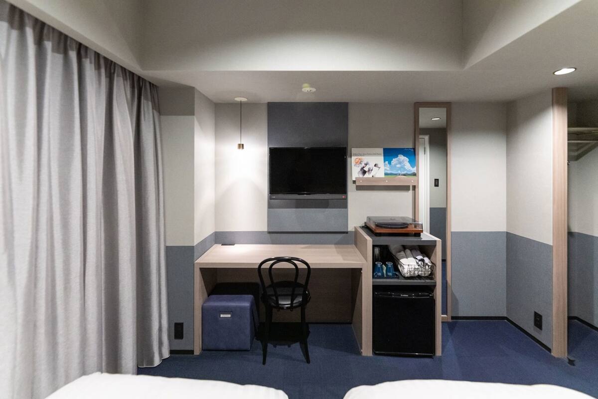 A hotel room with a desk, chair, TV, and a bed.