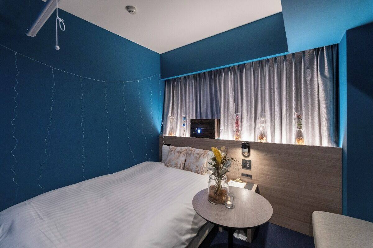 A hotel room with a bed, a small round table with a vase, and a window with curtains.