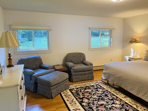 A bedroom with a bed, two armchairs, a dresser, and a rug.