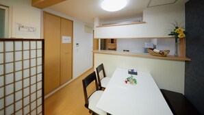 A room with a white table, two chairs, a wooden floor, a ceiling light, a wooden door, and a shelf with a vase of flowers. - Kyo Koyado Benten (Kyoto)