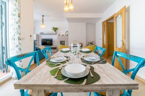 A dining area with a wooden table set for six, surrounded by blue chairs, and a kitchen in the background. - Chalet Parque Tecnológico, ideal for couples and families (Málaga)