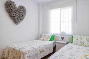 A bedroom with two beds, a heart-shaped wall decoration, and a window with blinds. - Chalet Parque Tecnológico, ideal for couples and families (Málaga)