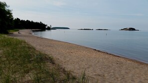 A beach with a sandy shore, calm water, and distant islands. - Charming East side-Marquette Home Convenient to Beach, Nmu & Hospital (Marquette)