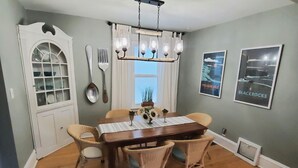 A dining room with a wooden table, wicker chairs, a chandelier, and wall-mounted cutlery. - Charming East side-Marquette Home Convenient to Beach, Nmu & Hospital (Marquette)