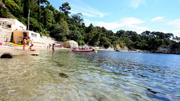 Una spiaggia con acque limpide e poco profonde, una barca gonfiabile rossa e persone che si godono la giornata.