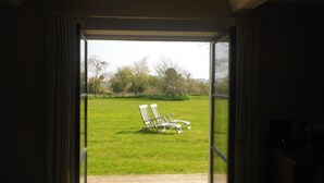 An open door leading to a grassy outdoor area with two white chairs.