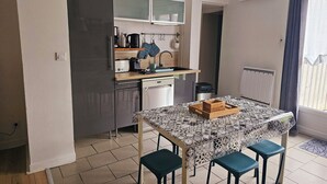 Een kleine keuken met een koelkast, fornuis, spoelbak en een eettafel met stoelen.
