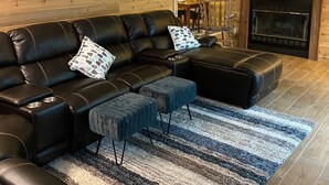 Un salon avec un canapé d’angle en cuir noir, une cheminée et un mur en bois sur lequel est accroché un panneau indiquant « LAKE ».