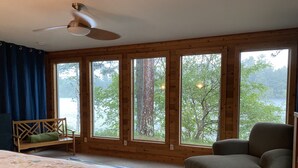 Une chambre à coucher avec un lit, une chaise, un canapé, de grandes fenêtres et un ventilateur de plafond.