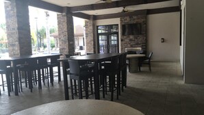 A spacious indoor area with a long table and chairs, a stone pillar, and a television mounted on the wall. - Welcome To Our Beautiful Villa In The Gorgeous Community Solterra! (Davenport)