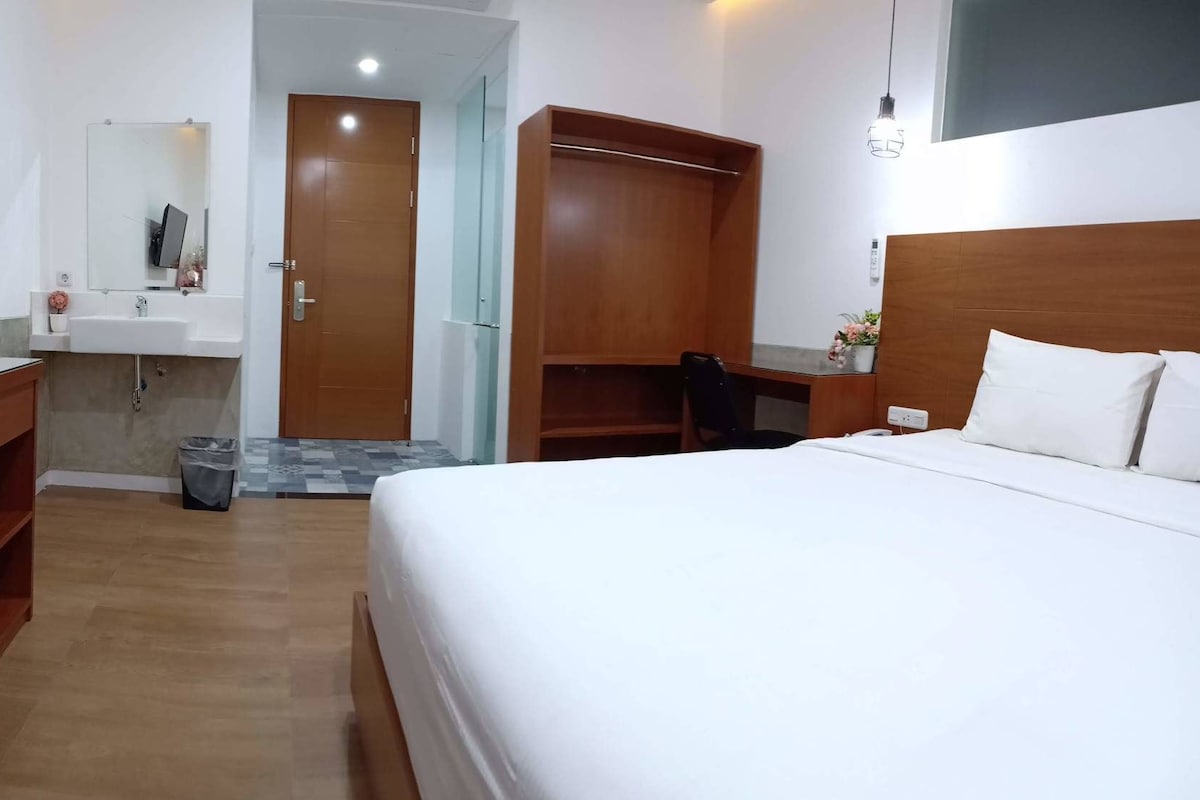 Una habitación de hotel con una cama, un escritorio, un armario, un espejo y un lavamanos.