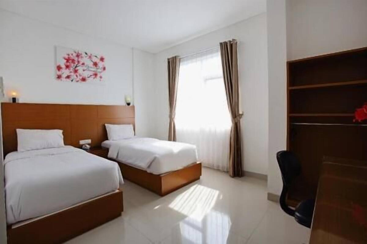 A hotel room with two beds, a desk, and a window with curtains.