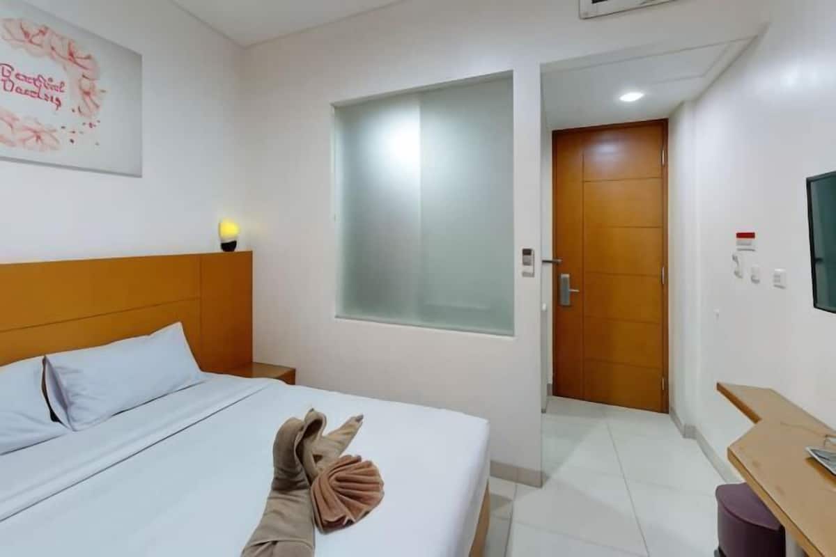 A hotel room with a bed, a desk, a chair, a window, and a door.