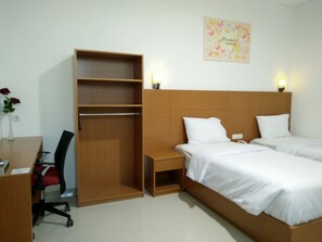 Une chambre d’hôtel avec une armoire en bois, un bureau avec une chaise, deux lits avec du linge de lit blanc et un luminaire fixé au mur.