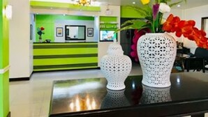 Un área de recepción con una decoración en tonos verde y blanco, un candelabro y dos jarrones blancos con flores.
