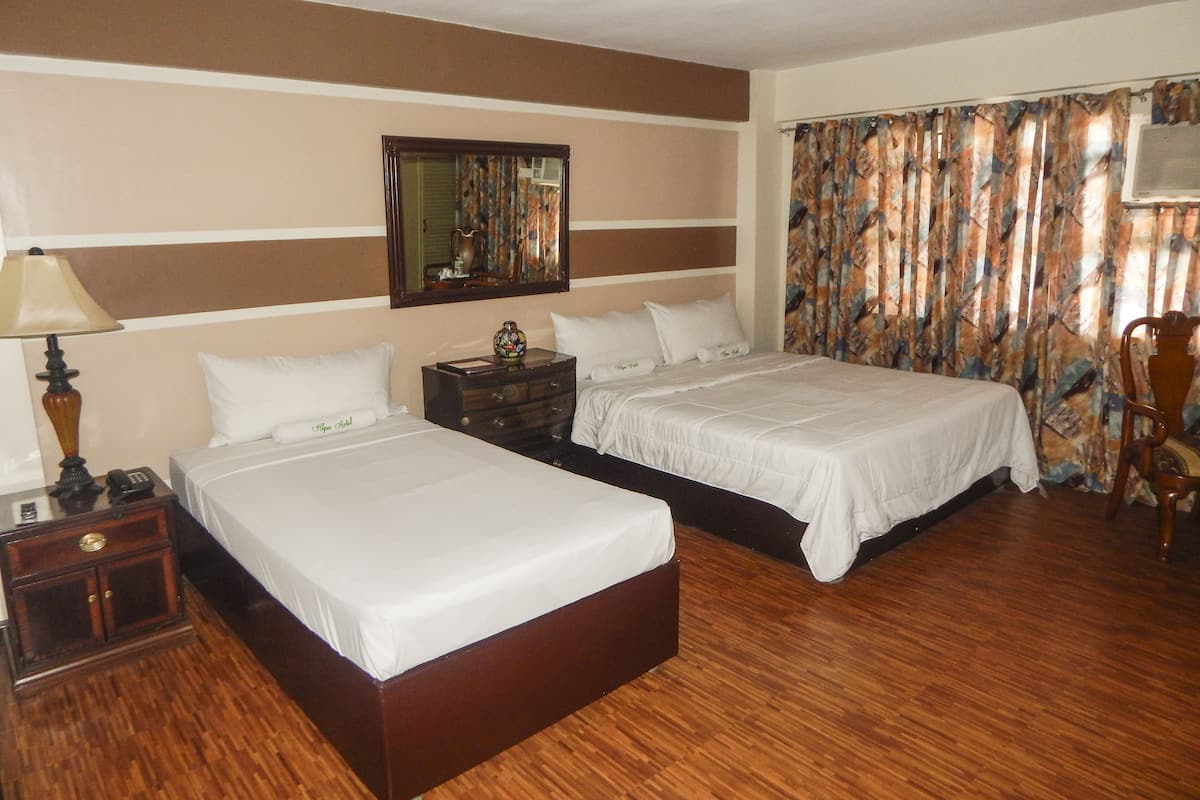 Een hotelkamer met twee bedden, houten vloeren, een nachtkastje met lamp, een dressoir en een spiegel aan de muur.