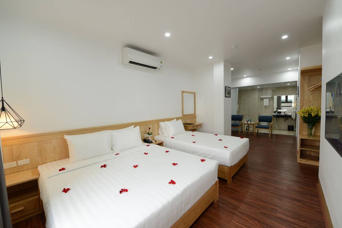 A hotel room with two beds, wooden headboards, a bedside table, a nightstand, a desk, a chair, a small table, a mirror, and an air conditioning unit.