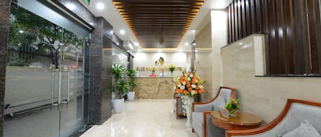A hotel lobby with a reception desk, seating area, and a large potted plant.