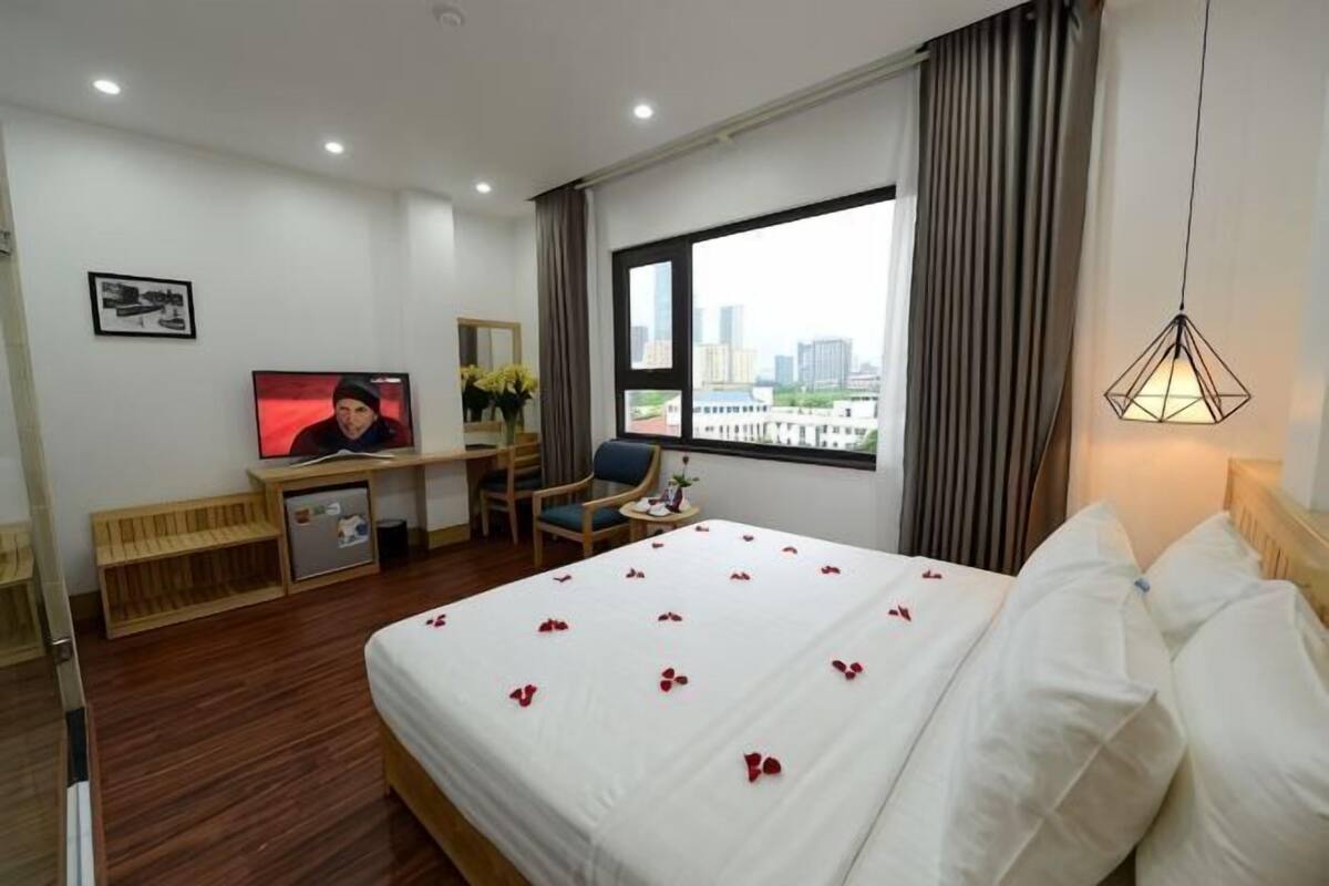 A hotel room with a bed, a desk with a television, a chair, a window with curtains, and a city view.