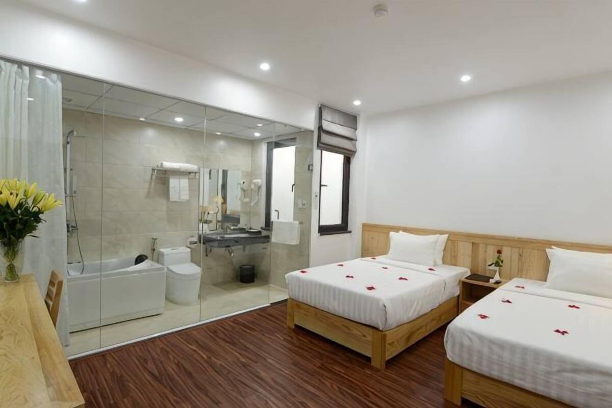 A hotel room with two beds, a bathroom, and a glass-enclosed shower area.