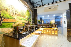 A modern hotel lobby with a marble floor, a buffet area with various food items, and a mural of a landscape. - Blue Hanoi Inn City Hotel (Hanoi)