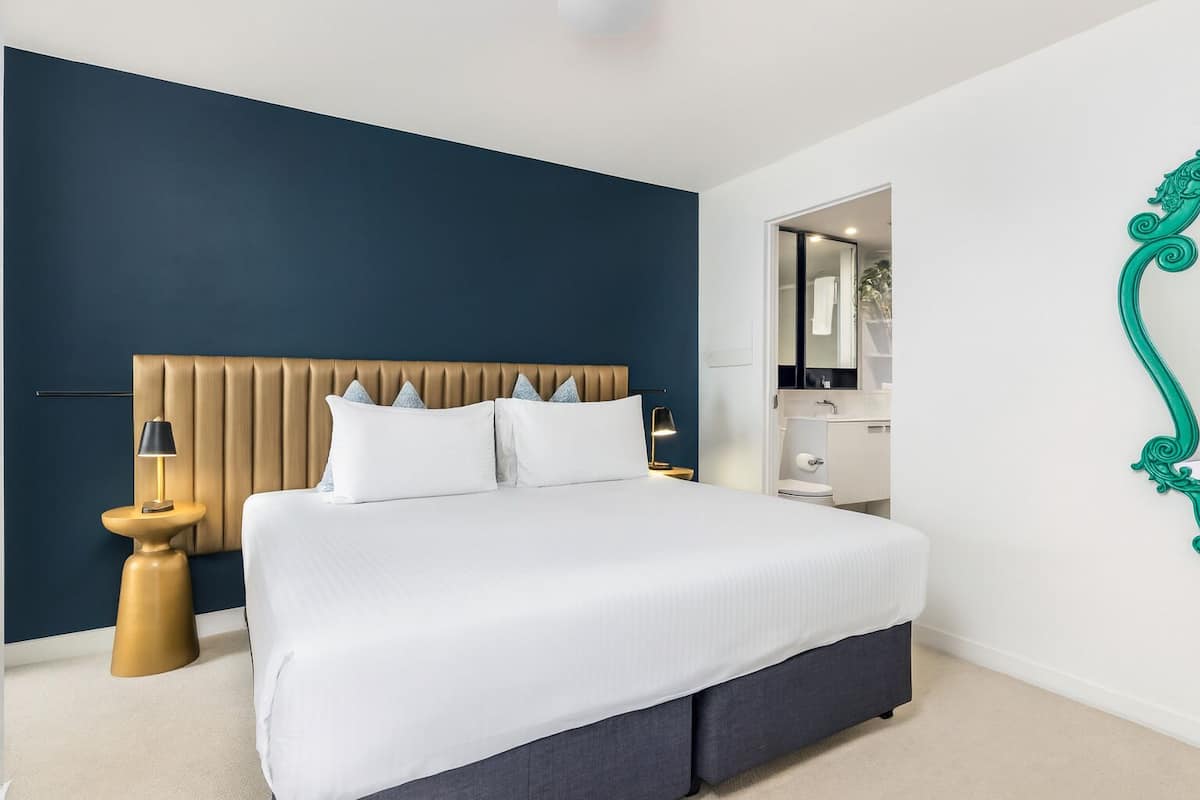 A modern bedroom with a large bed, a wooden headboard, a nightstand, a lamp, and a mirror.