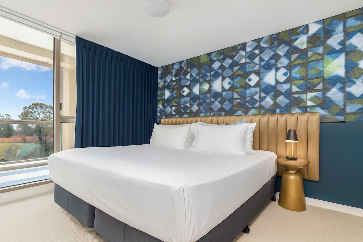 A modern hotel room with a large bed, a view of the outdoors, and a geometric-patterned wall.
