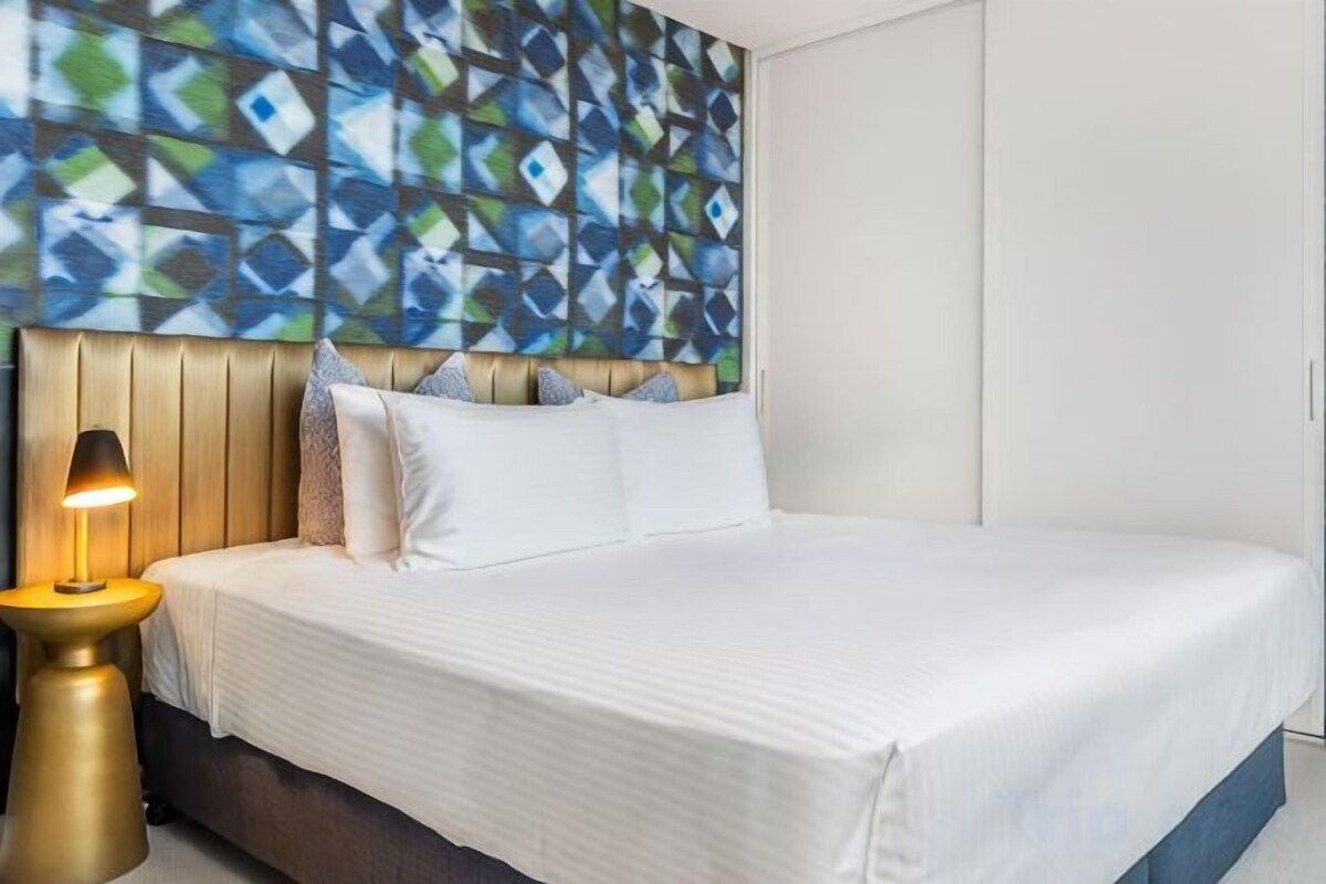 Een netjes opgemaakt bed met witte lakens, een houten hoofdbord en een bedlampje.