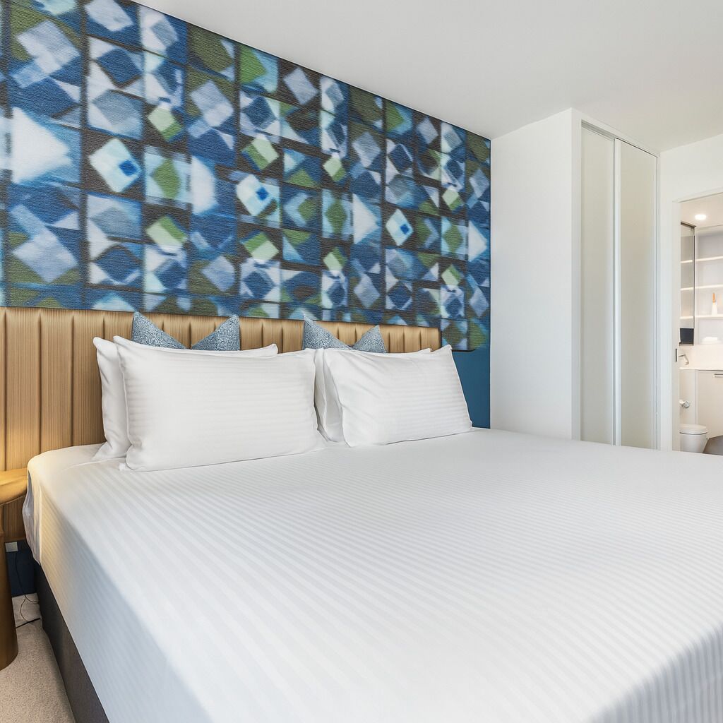 A hotel room with a large bed, a wooden headboard, and a geometric-patterned wall mural.