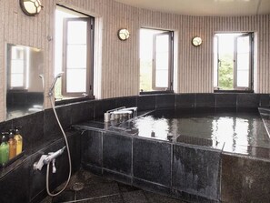 Une salle de bain moderne dotée d’un grand bain à remous rectangulaire, d’une zone de douche et d’un lavabo avec des articles de toilette.