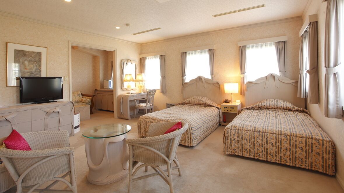 A hotel room with two beds, a television, a desk with a chair, and a small table.