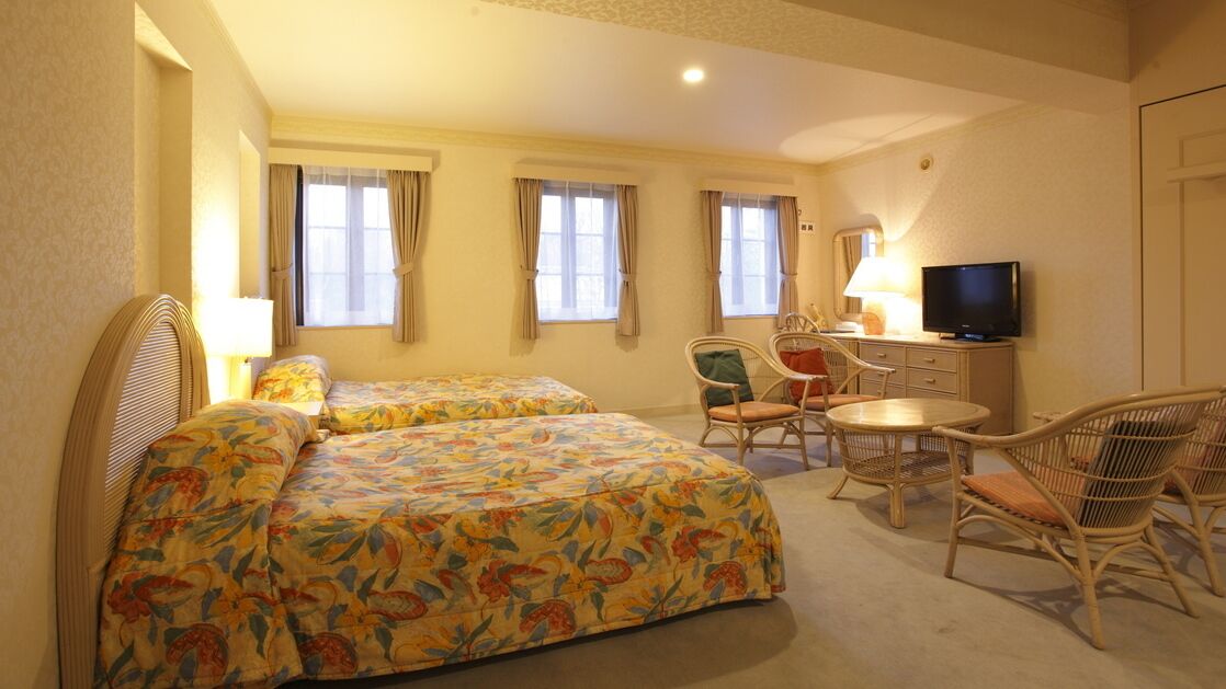 A hotel room with two beds, a television, a desk with a chair, and a window with curtains.