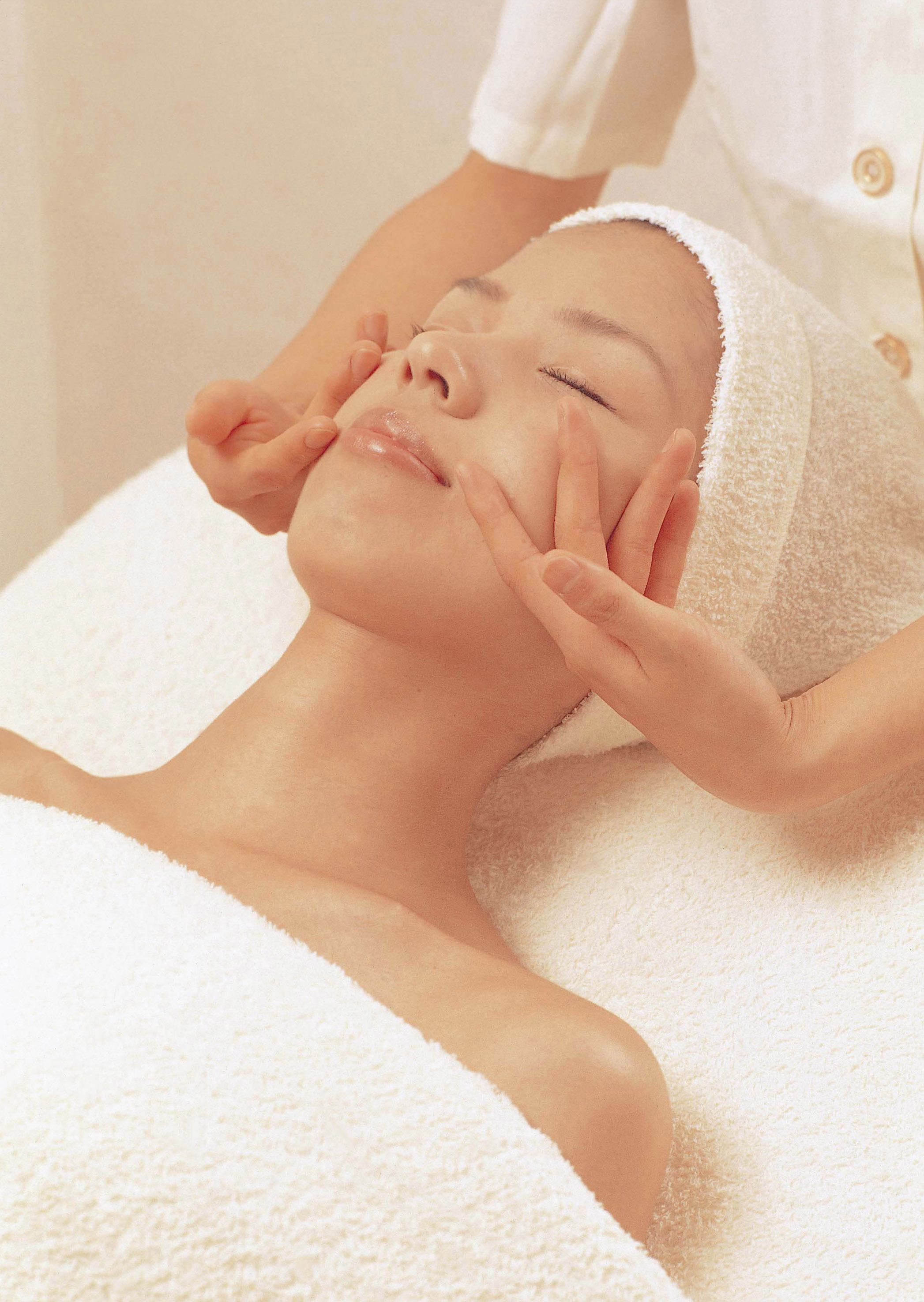 Una persona recibiendo un tratamiento facial, acostada sobre una superficie cubierta con una toalla blanca.