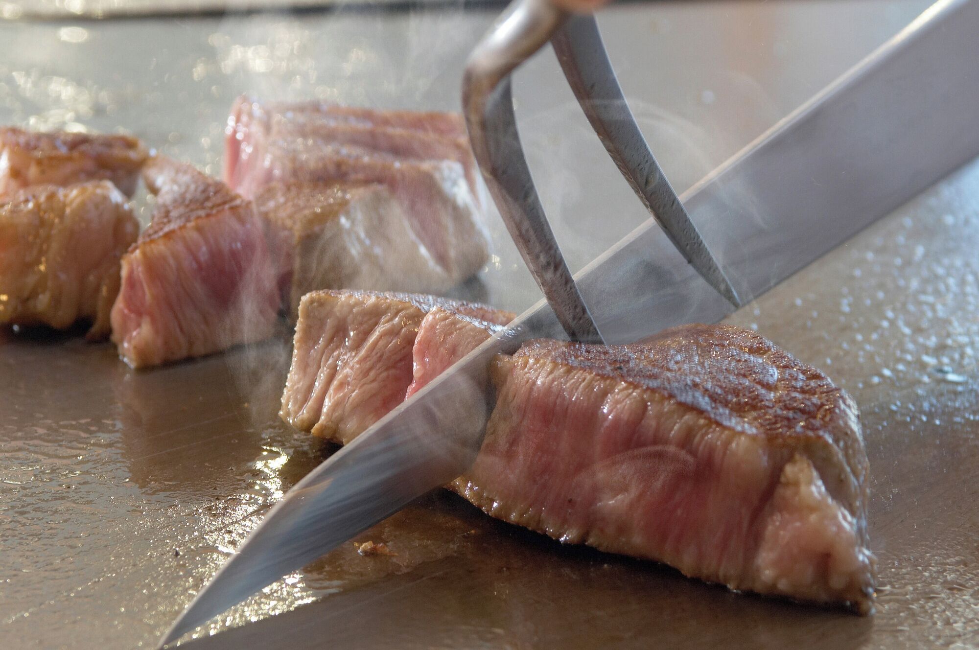 A close-up of a steak being sliced on a grill.