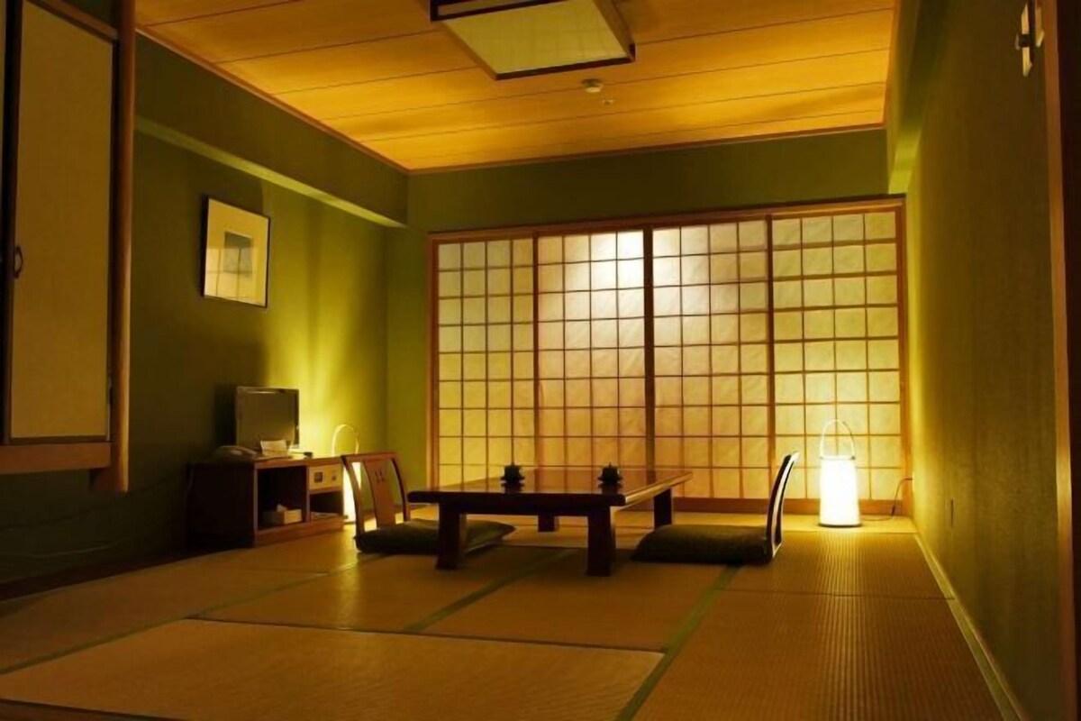 Et rum med tatamimåtter, en shoji-skærm, et lavt bord, en stol og en traditionel japansk lampe.