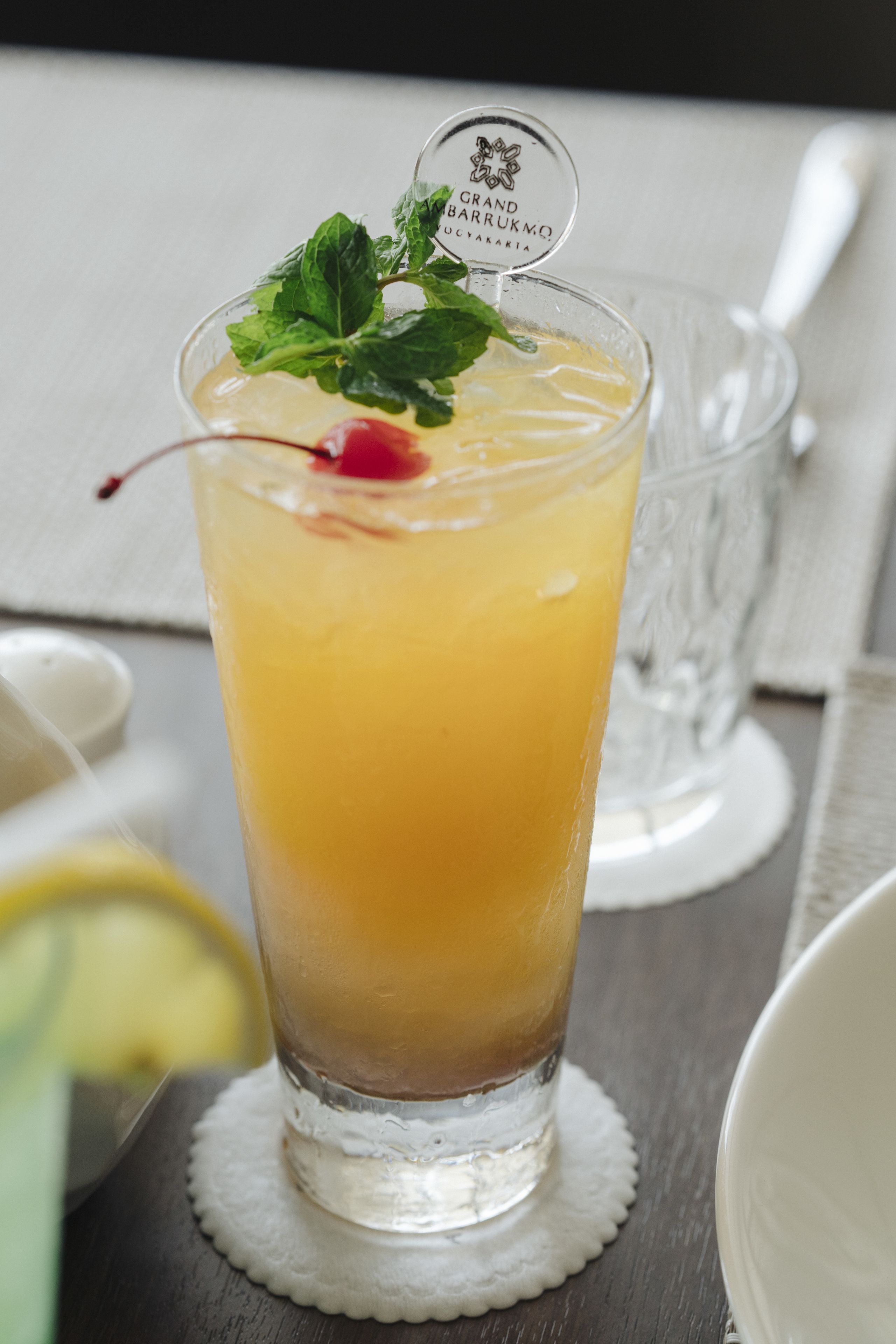 A tall glass of a layered beverage with a cherry and mint garnish, placed on a white coaster.