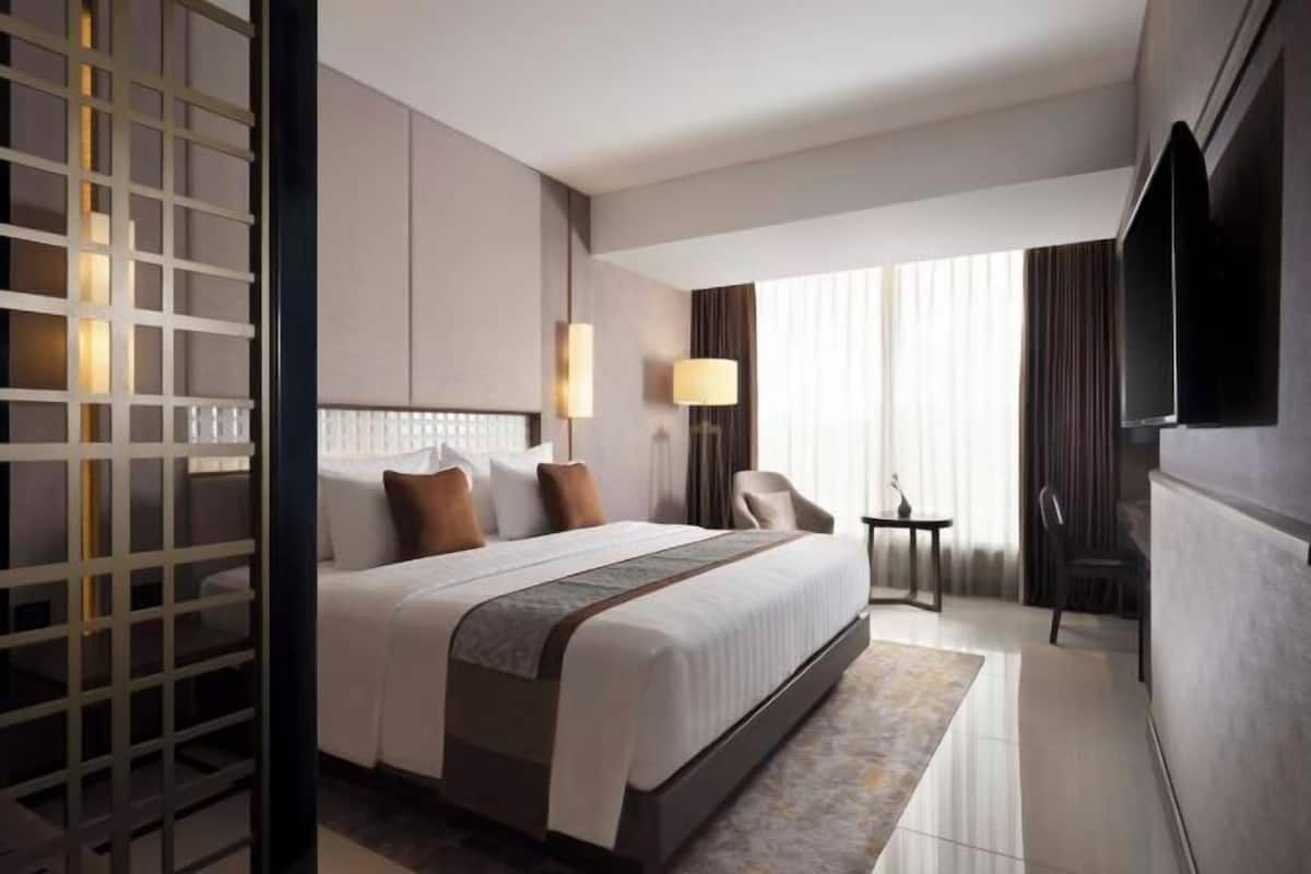 Ein Hotelzimmer mit einem großen Bett, einem Fernseher, einem Schreibtisch und einem Sessel.