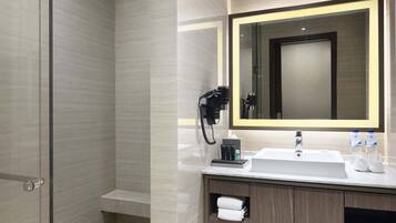 A modern bathroom with a glass shower enclosure, a large mirror with a lighted frame, a sink with a countertop, and a towel rack.