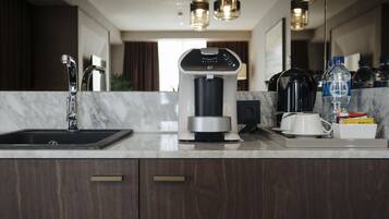 Una cocina moderna con cafetera integrada, un lavamanos y una encimera con diversos objetos, incluyendo una botella de agua y una jarra de café.