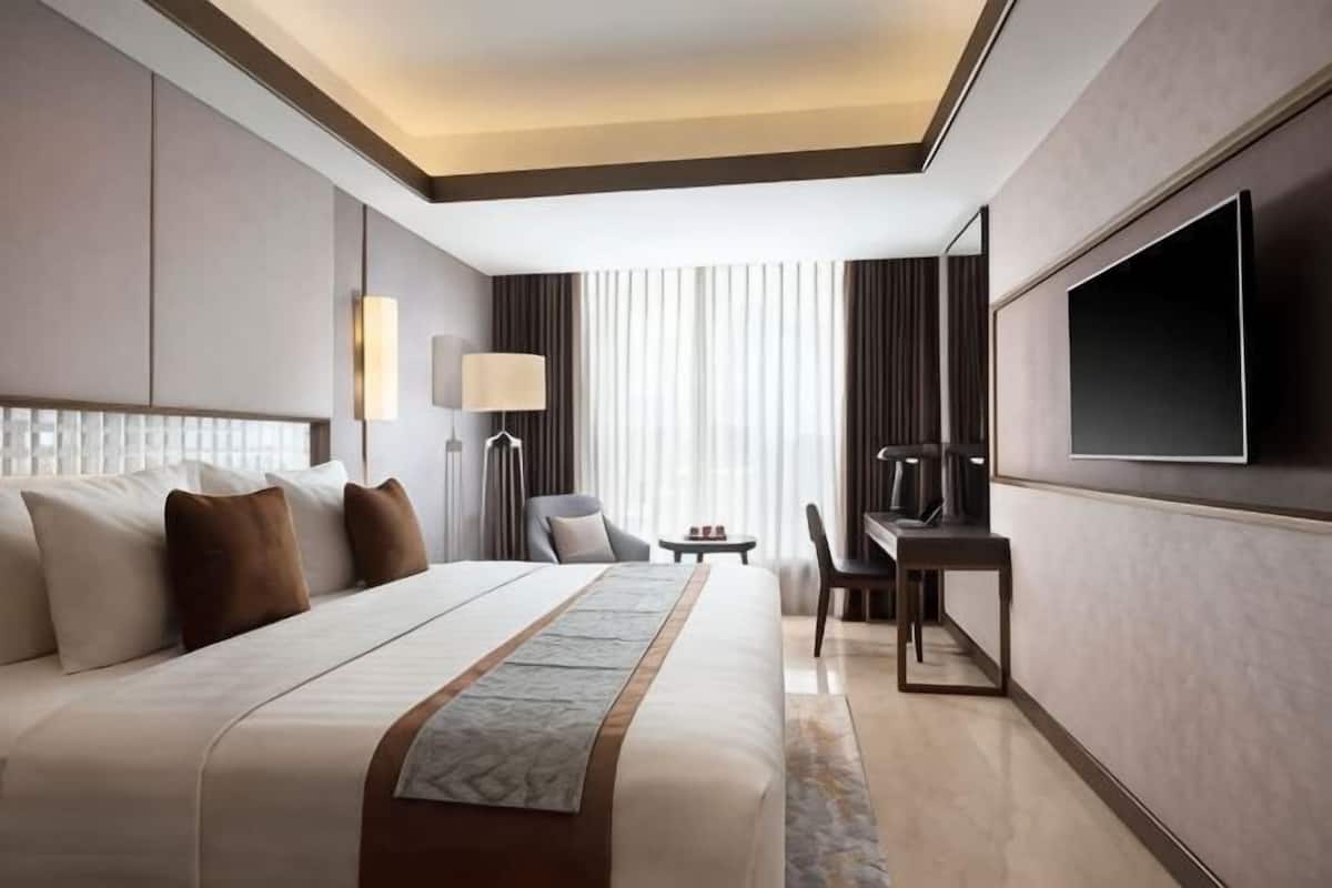 Ein modernes Hotelzimmer mit einem großen Bett, einem Schreibtisch, einem Sessel, einem Fernseher und einer Lampe.