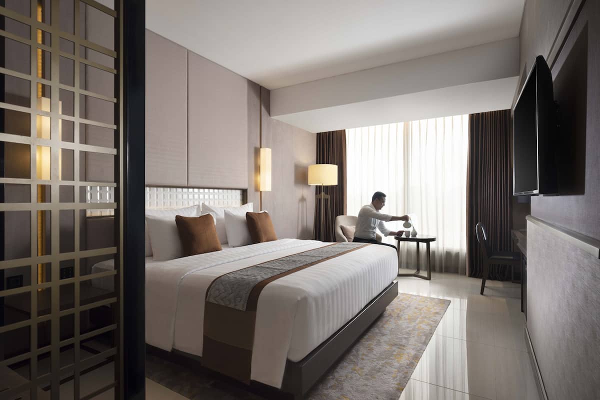 A hotel room with a large bed, a desk, a television, and a view of the city.