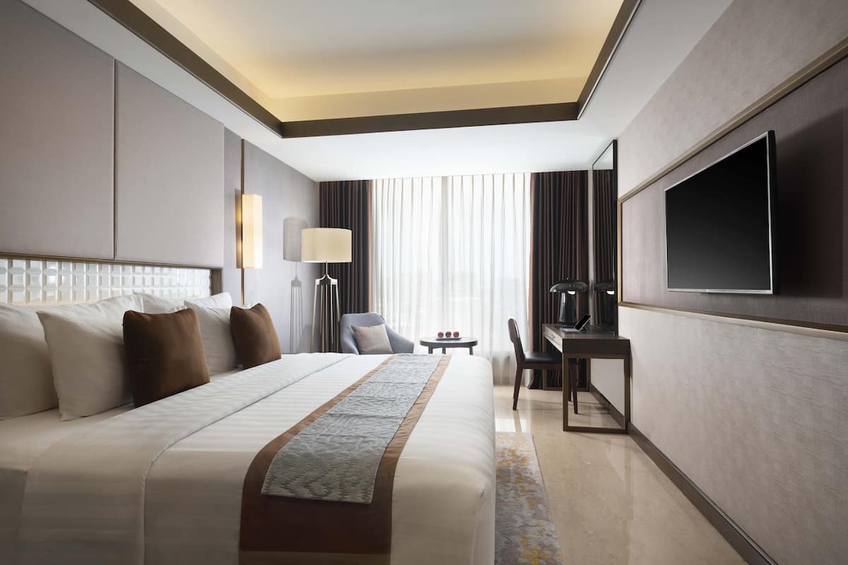 A hotel room with a large bed, a desk, a TV, and a window with curtains.