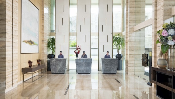 Un área de recepción moderna con techo alto, un cuadro abstracto grande y un mostrador de recepción con tres empleados.
